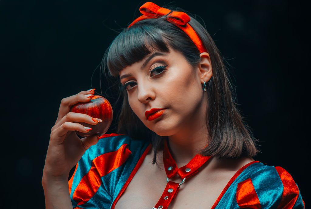 Young woman dressed as Snow White holding a red apple in a studio setting, evoking classic fairytale imagery.